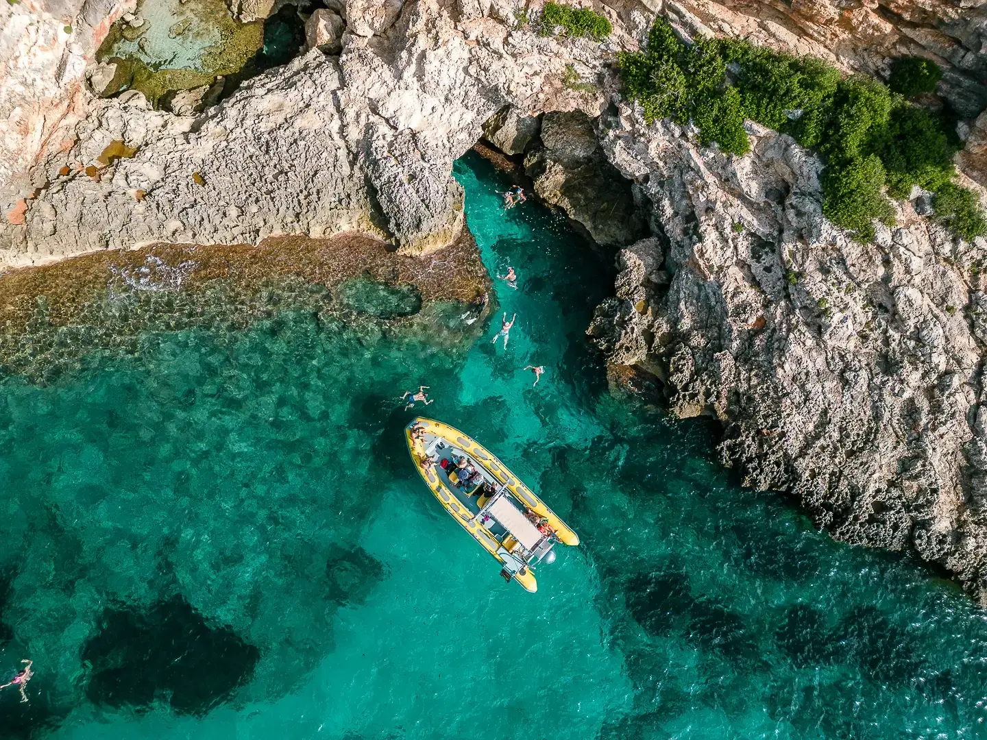 A Skualo boat and swimmers exploring a turquoise cove in Mallorca